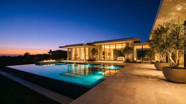 A modern backyard at dusk — a fire pit, layered planting and a lit pavilion